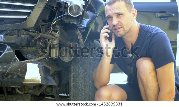 car accident\
concept. male driver makes phone calls after a traffic accident\
sitting by a broken car\
bumper