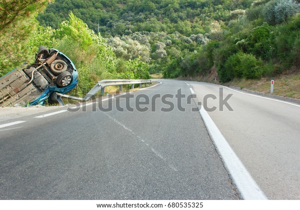 car accident on a mountain forest road.\
Turned upside-down the broken car pulled off the road and fell into\
a ravine. Asphalted mountain forest\
road