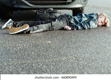 Car Accident - Young Teenage Boy Has Been Hit by Car and is Lying Injured, Unconscious or Dead on Pavement in front of Tires of Car, with Foreground Copy Space - Powered by Shutterstock