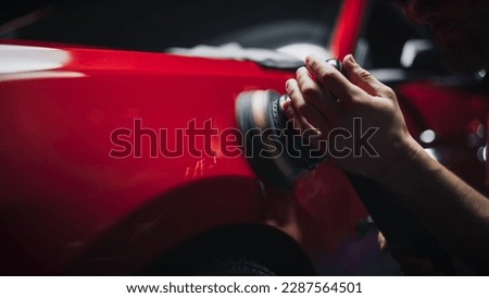 Car Ad Style Photo of a Professional Car Detailer Using an Electric-Powered Polishing Machine to Work on a Fender of a Beautiful Red Sportscar After Washing and Detailing the Vehicle