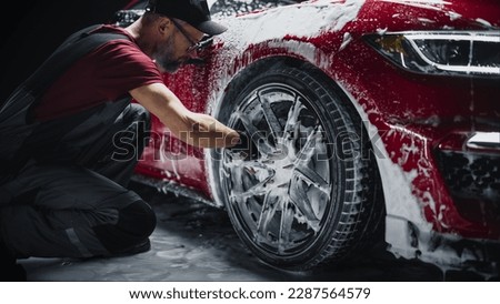 Car Ad Style Photo of a Professional Car Wash Specialist Using a Big Soft Sponge to Wash the Rims of a Beautiful Red Sportscar with Shampoo Before Detailing, Polishing and Waxing