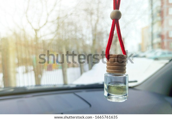 Car air freshener\
hanging on a lace. Freshener on the rearview mirror. Close-up on a\
windshield background.