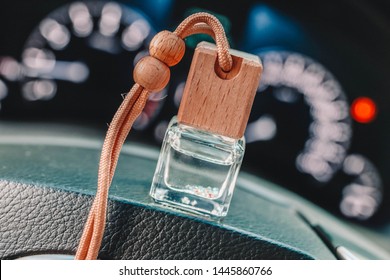 Car air perfume freshener bottle inside the car on the steering wheel. Little glass bottle with wooden lid and aromatic liquid on the blurred background with dashboard lights.