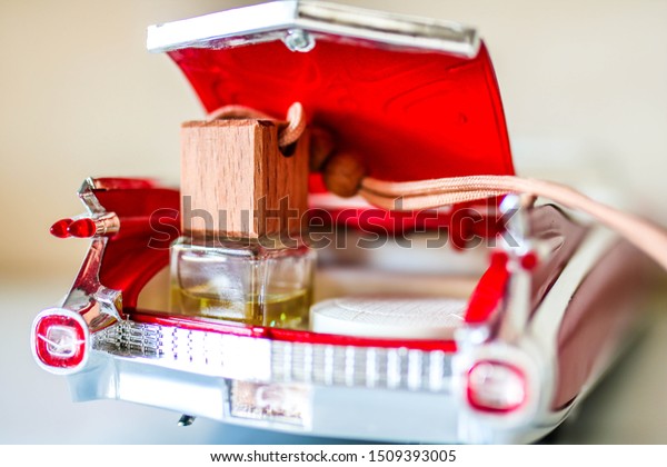 Car air perfume freshener bottle in the trunk of\
a toy car on white plastic table. Little glass bottle with wooden\
lid and aromatic liquid.