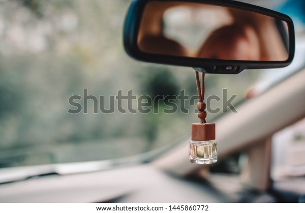 Car air perfume\
freshener inside the car with blurred green background. Little\
glass bottle with wooden lid and yellow aromatic liquid automobile\
freshener on car mirror.