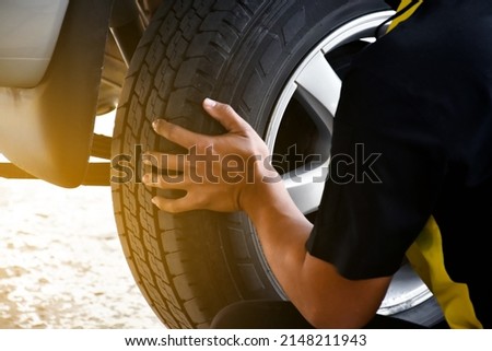 The car attendant  is turning the car wheel back into the car's hub after the tire leak has been repaired, soft and selective focus on wheel, in motion.