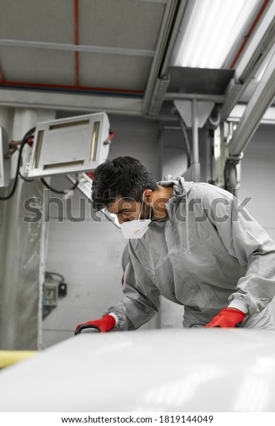 car, auto detailing. young auto mechanic\
man work with the use of orbital polisher, in auto repair shop,\
wearing uniform, protective mask and\
gloves