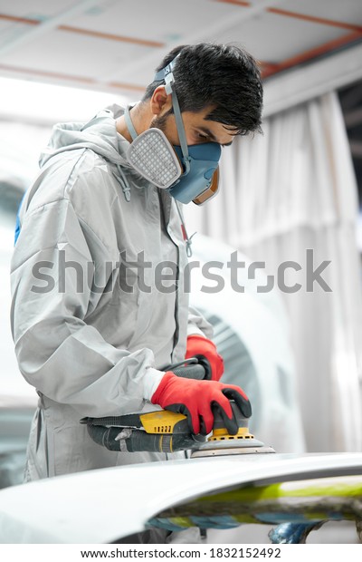 car, auto detailing. young auto mechanic\
man work with the use of orbital polisher, in auto repair shop,\
wearing uniform, protective mask and\
gloves