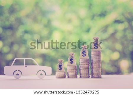 Car or auto loan, cash repayment, financial concept : White model sedan car and rows of rising coins with dollar bags, depicts saving money to buy a new car, or making down payment for second hand car