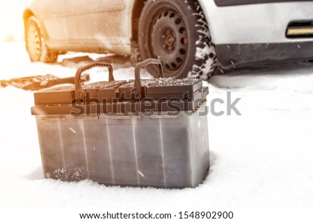 Car battery against the background of a car in winter. Winter battery discharge concept, copy space