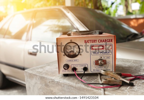 Car battery charger over blurred car\
background, outdoor day light, old charger with old\
car