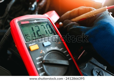 Car battery voltage testing with a digital multimeter by auto technician, Car voltage current display on black screen of digital multimeter, Car maintenance service concept