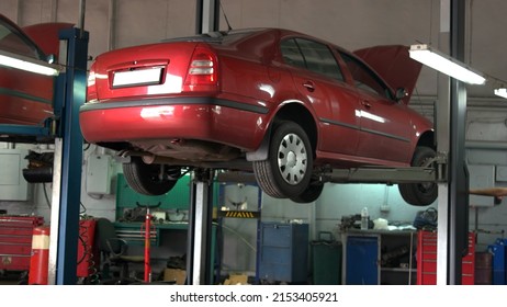 Car is being lifted down by hydraulic machine for technician. Close-up red car with opened hood. - Shutterstock ID 2153405921