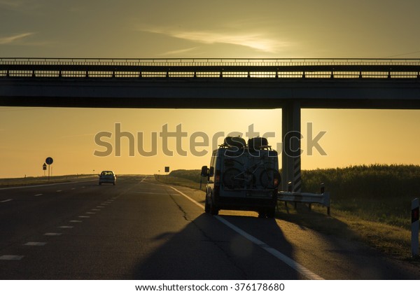 Car with bicycles on\
the road at sunset.