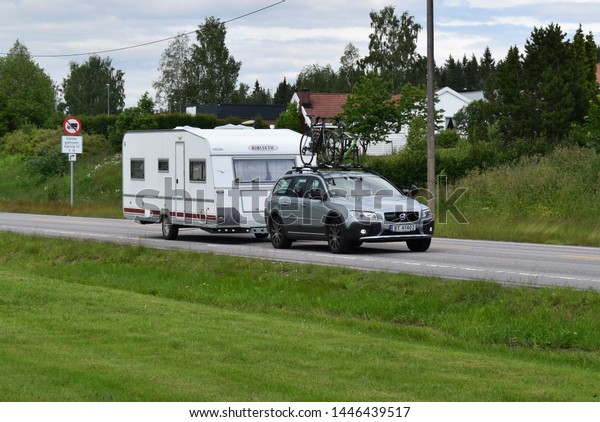 Car with bicycles on the roof and\
Bjølseth Caravan travel summer vacation road trip - sunny and\
summer season - Kongsvinger, Norway (26th june\
2019)
