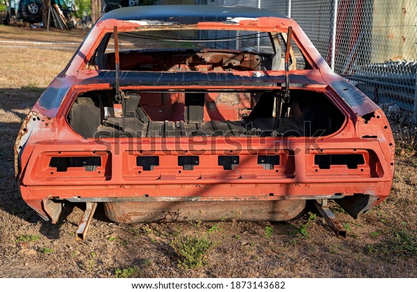 A car body\
frame discarded in a country\
backyard