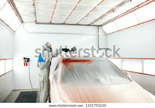Car body painter spraying paint in garage or\
workshop with airbrush