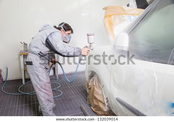 Car body painter spraying paint\
or color on bodywork in a garage or workshop with an\
airbrush