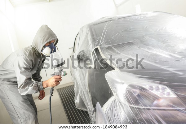 Car body worker paints a car in the\
paint booth with a spraying paint and a protective\
mask