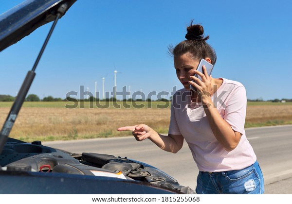 Car breakdown, unhappy woman on the road with open\
car hood talking on the mobile phone. Car repair service,\
transportation, tow truck\
call
