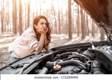 The car broke down. Accident on the road. The woman opened the hood and checks the engine and other parts of the car. She is looking at the camera and does not know what to do.