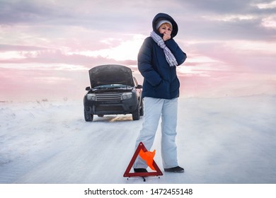 The Car Broke Down On The Road. The Woman Warms Her Cold Hands. She's Cold. Winter. Emergency Stop Sign. Around A Snowy Field.