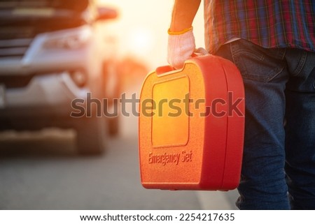 Car broken on the road. Man holding red emergency tools box and standing infront of car on the roadside. Car accident, repair and maintenance concept