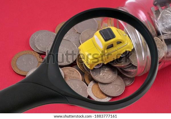 Car budget concept with a magnifying glass over a jar\
of money and a car