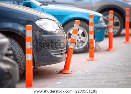 Car bumper and bent flexible plastic bollard in parking lot. Broken flexible traffic bollard. Car bumper and plastic barrier closeup. Car parked close to orange reflective bollard.