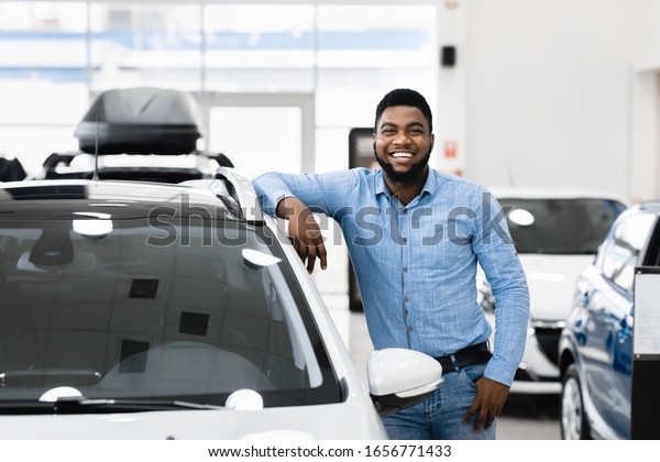 Car Buyer. Happy Afro Man Standing\
Posing Near New Auto In Dealership Store. Copy\
Space