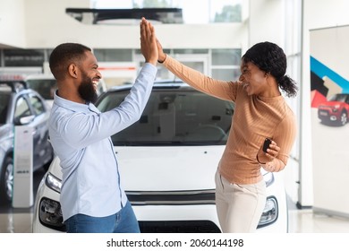 Car Buyers. Excited Black Spouses Celebrating Purchasing New Vehicle In Dealership Center, Happy African American Couple Giving High Five To Each Other After Buying Automobile In Showroom