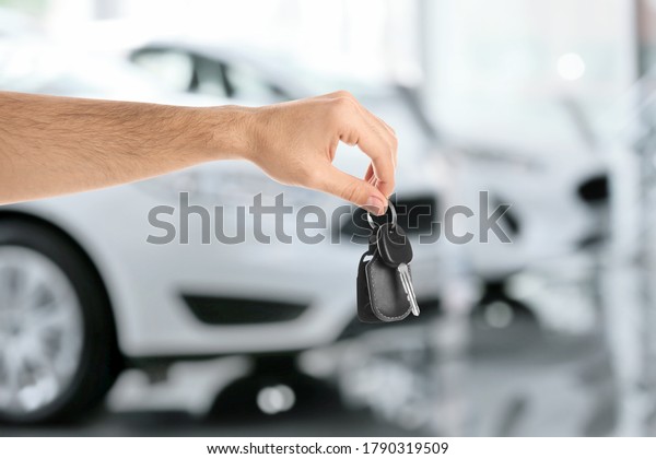 Car buying. Man holding key against blurred\
automobiles, closeup