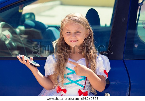 Car calling\
taxi app searching concept. Little girl kid child showing at the\
phone screen standing near a blue\
car