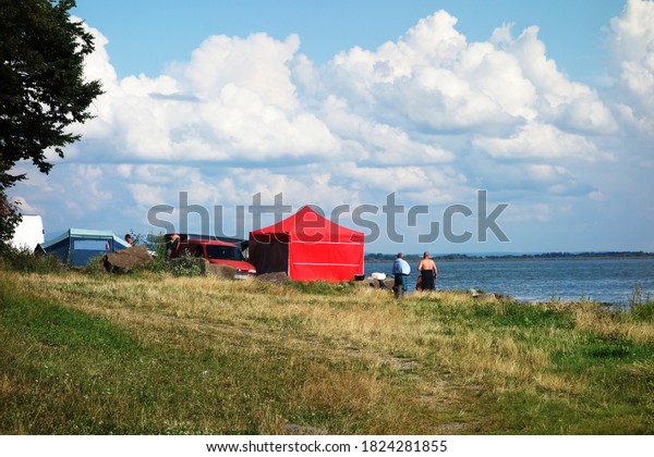 Car camp with tents on the grassy beach by the\
lake in the summer season