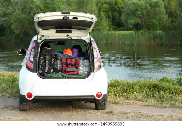 Car with camping equipment in trunk on riverbank.
Space for text