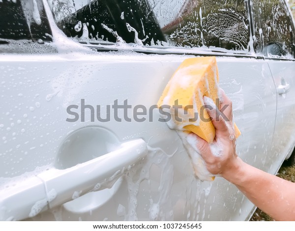 Car Care business  Washing white car\
surface with yellow sponge and full of bubble\
foam.
