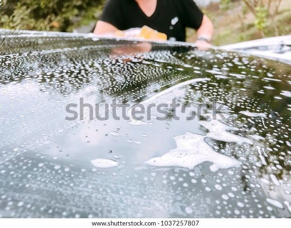 Car Care business, Washing white car\
windshield with yellow sponge and full of bubble\
foam.