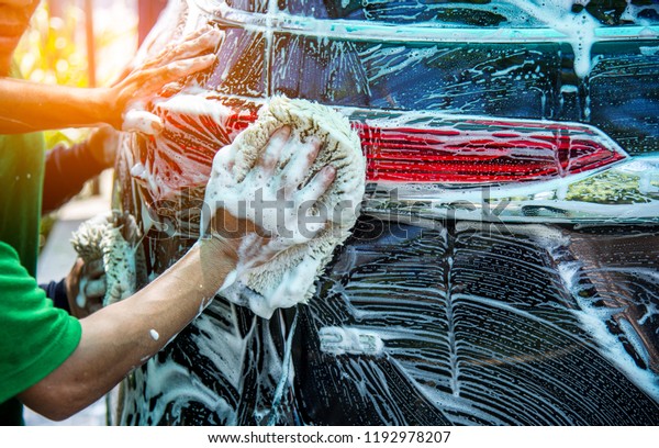 Car care worker hand holds sponge with foam\
car wash to clear  outsides of the\
car.