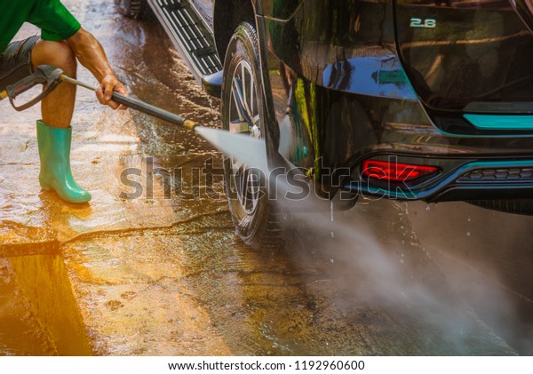 Car care worker wash a car with high pressure\
washer outside car wheels for\
clean