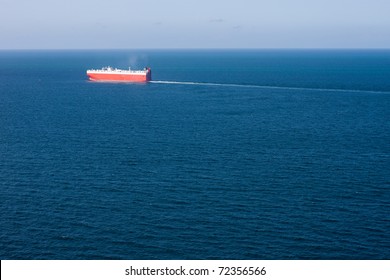 A Car Carrier Cargo Ship Sails A Deep Blue Vast Ocean, Leaving A Think Wake Behind.  Horizontal Image With Deep Vessel.