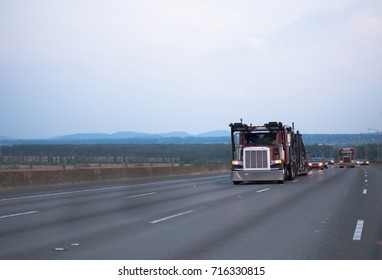 A car carrier on a large classic American big rig semi truck with a two-tier trailer for the transport of cars goes on a multi-lane highway in the evening twilight towards the loading point