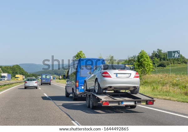 Car carrier trailer with car.\
Blue minibus with tow truck transporter carrying car on\
highway