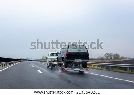 Car carrier trailer with car on wet road. Spray from under the wheels of car