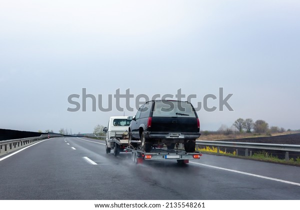 Car carrier trailer with car on wet road. Spray\
from under the wheels of\
car