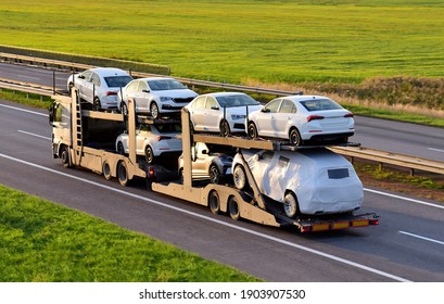 Car carrier trailer transports cars on highway on sunset background. Auto transport and car shipping services concept. Truck with Semi-remorque. Cars Shipping. Car transportation