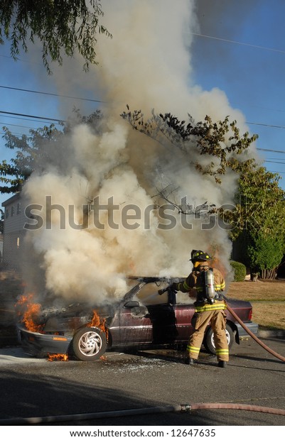 A car caught on fire in the street and
firefighters work on putting out the
fire.