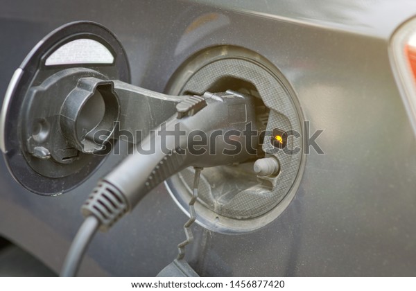 Car charging on charge station in the center of\
the city. Charge port, connector and cable. Electric Car Charger.\
Close-up power supply plugged into electric car being charged -\
alternative energy
