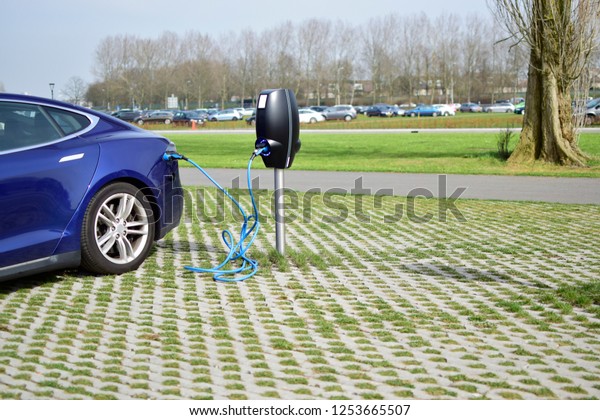 Car charging power battery. Charging power
station with electricity battery sign for electric car, cable and
plug in nature and street background.

