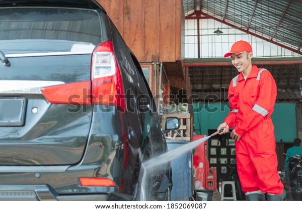 A car cleaner using a\
red uniform sprays high pressure water using a hose onto the tires\
in the car wash