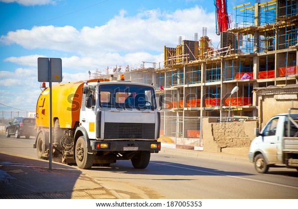 Car cleans the road from the dust.\
construction of a building in the\
background